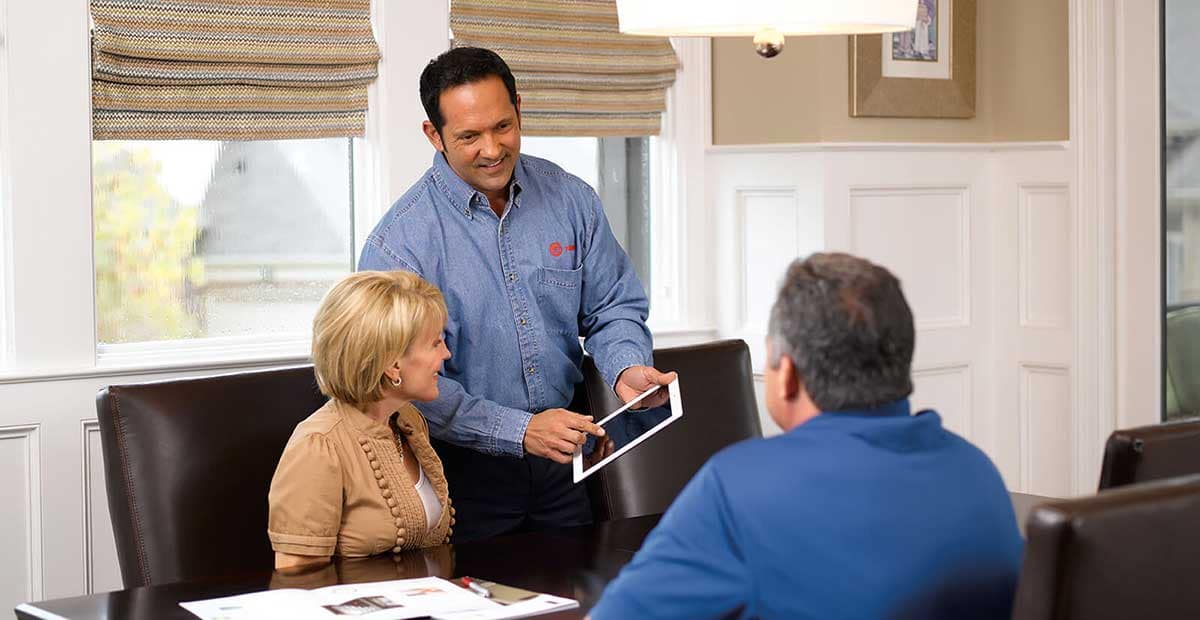 Trane comfort specialist with homeowners presenting hvac & electrical services options on ipad