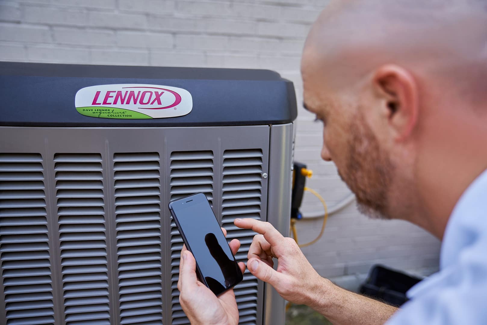 HVAC technician using a smartphone to diagnose a Lennox air conditioning unit during service for Deals Heating & Air.